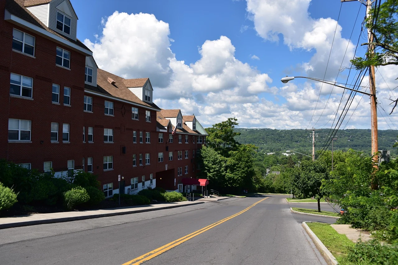 A sloping Ithaca street with brick buildings, green hills and a blue sky